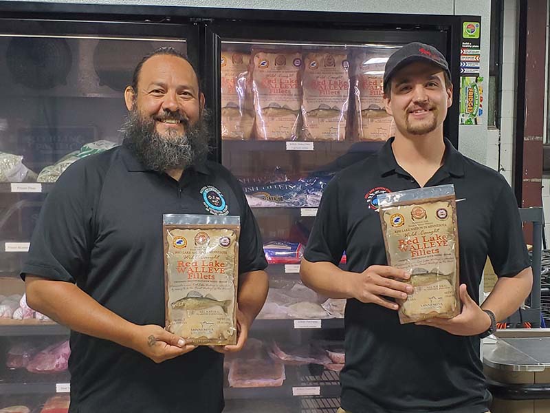 two men holding packaged frozen fish in front of FDPIR store freezer