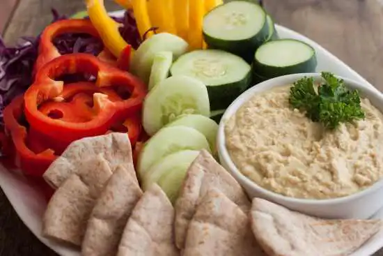 platter with a bowl of hummus and sliced veggies