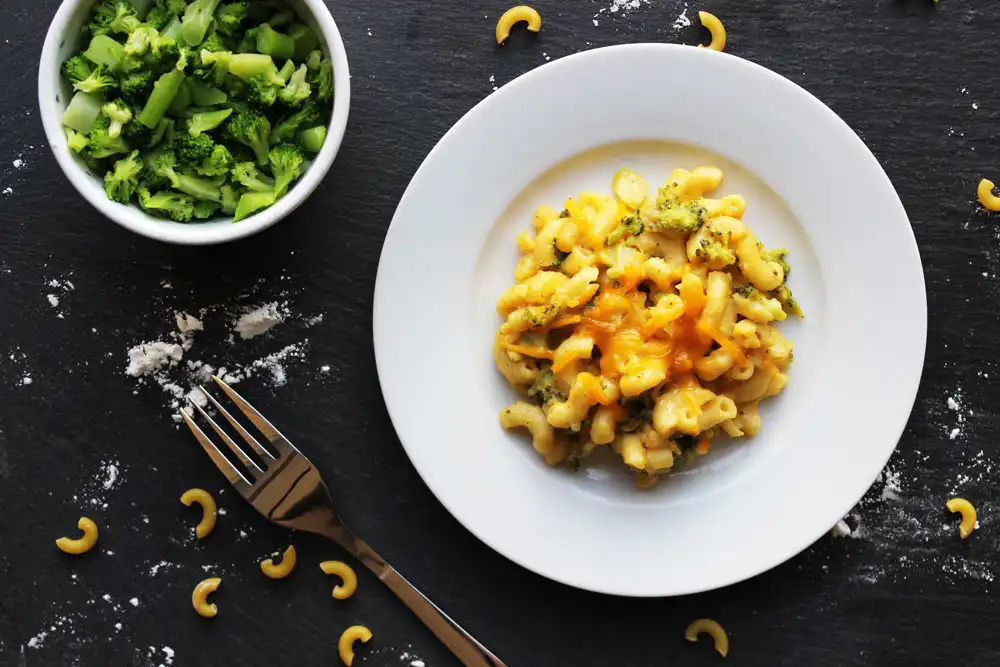 white bowl of macaroni and cheese with a side bowl of broccoli
