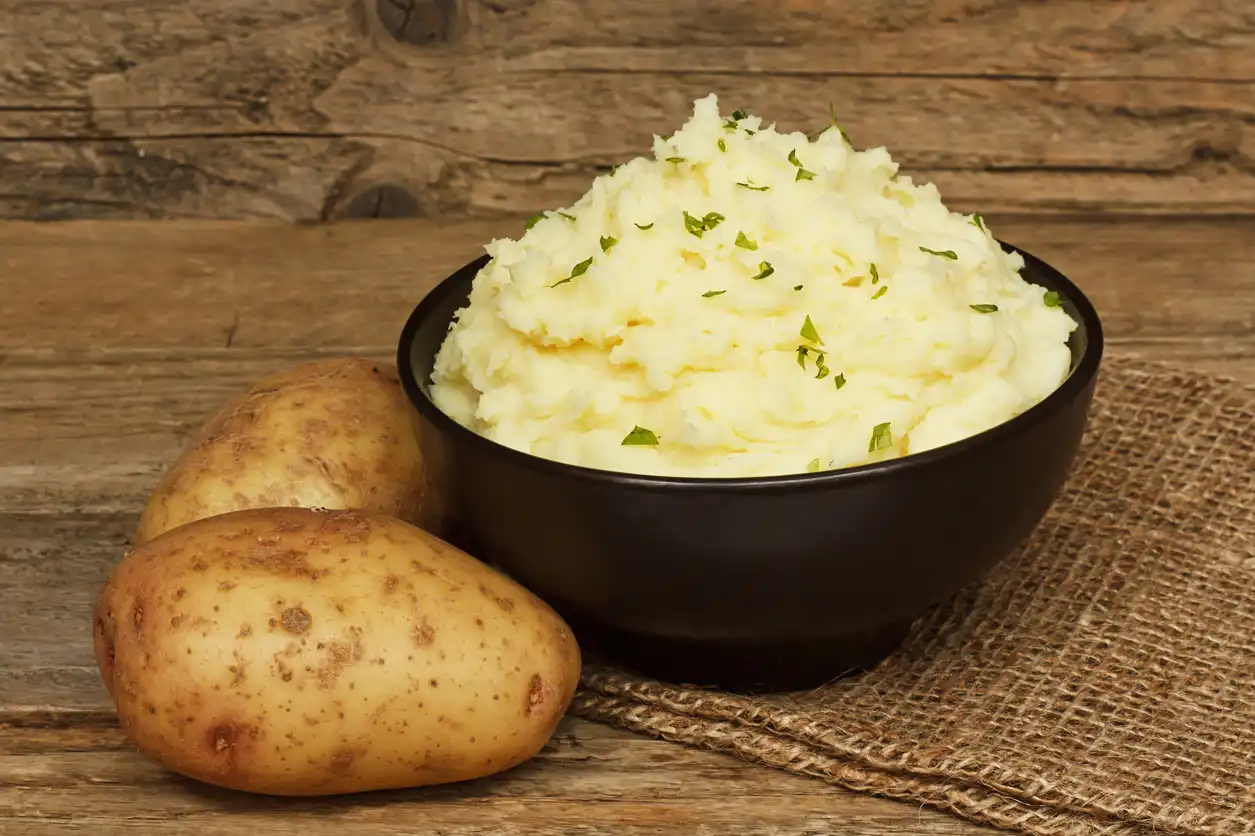 black bowl of mashed potatoes with two whole potatoes next to it