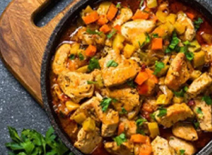 a skillet with prepared food and vegetables on a wooden cutting board