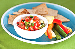 A plate of vegetables, chips and a cup of salsa