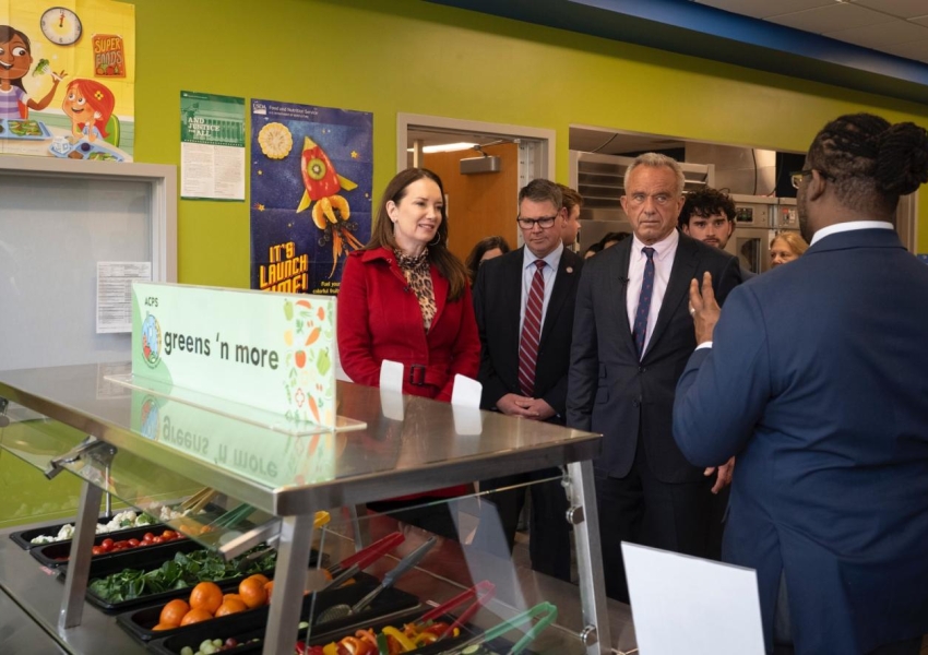 USDA and HHS secretaries at MAHA event in front of a salad bar in a school cafeteria.