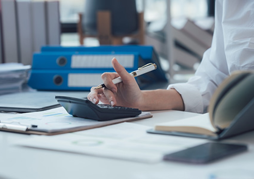 hand typing into a calculator at a desk surrounded by papers and notebooks