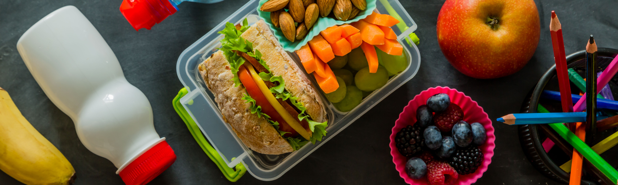a boxed lunch next to a milk bottle an apple, and a bowl of berries