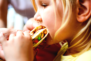 Young girl eating a tortilla with meat and vegetables