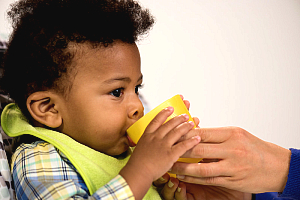 Infant drinking from a cup with assistance
