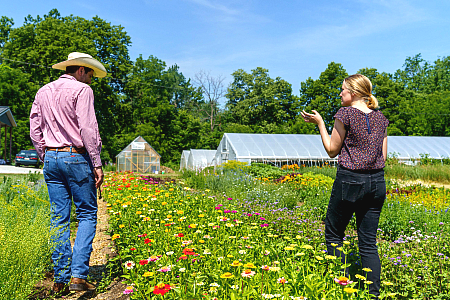 A woman walking through a field of flowers with a farmer asking questions and seeing the farm.