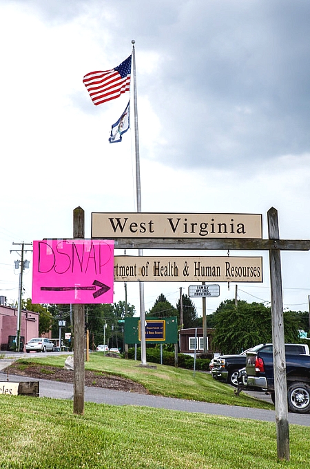 a sign saying West Virginia with an American Flag and a pink posterboard saying "D-SNAP" with an arrow