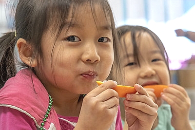 two girls eating orange slices and smiling
