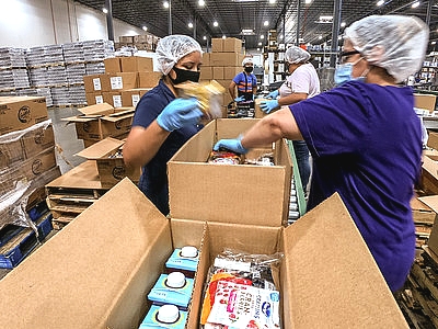women in a warehouse wearing hair nets packing food boxes
