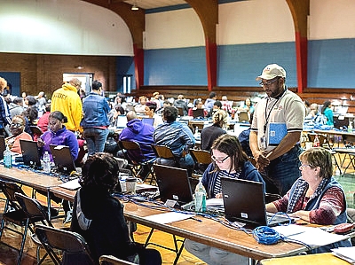 a school gymnasium with tables set-up for disaster response efforts with staff at laptops
