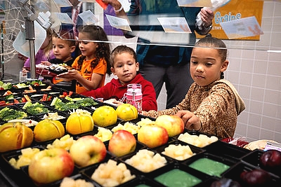 kids in a school lunch line with a girl reaching for an apple