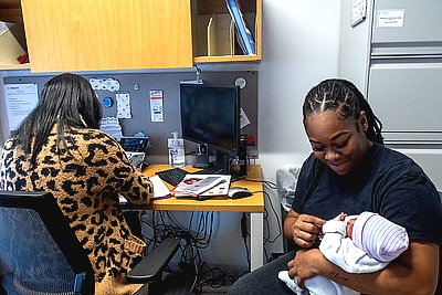 an image of a WIC staff person at a desk doing paperwork next to a mother and her infant in her arms