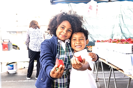 Two happy children holding strawberries at a farmers' market.
