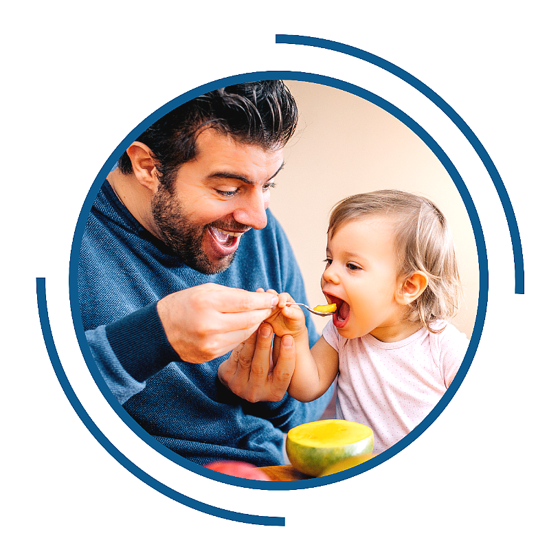 A dad energetically feeding his young child.